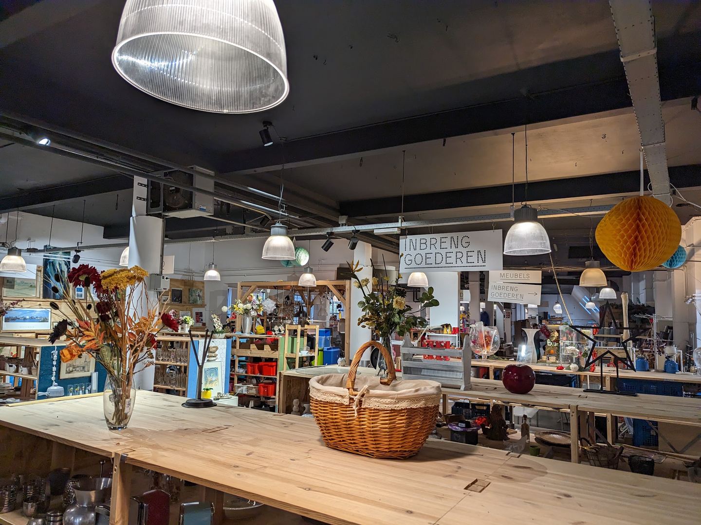 Interieur van RataPlan met houten tafels, hanglampen en rekken vol tweedehands spullen