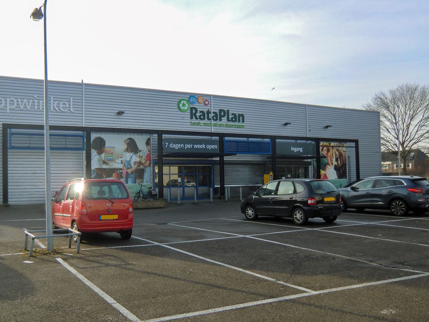 Gevel van de RataPlan-kringloopwinkel met logo, ingang en parkeerterrein ervoor