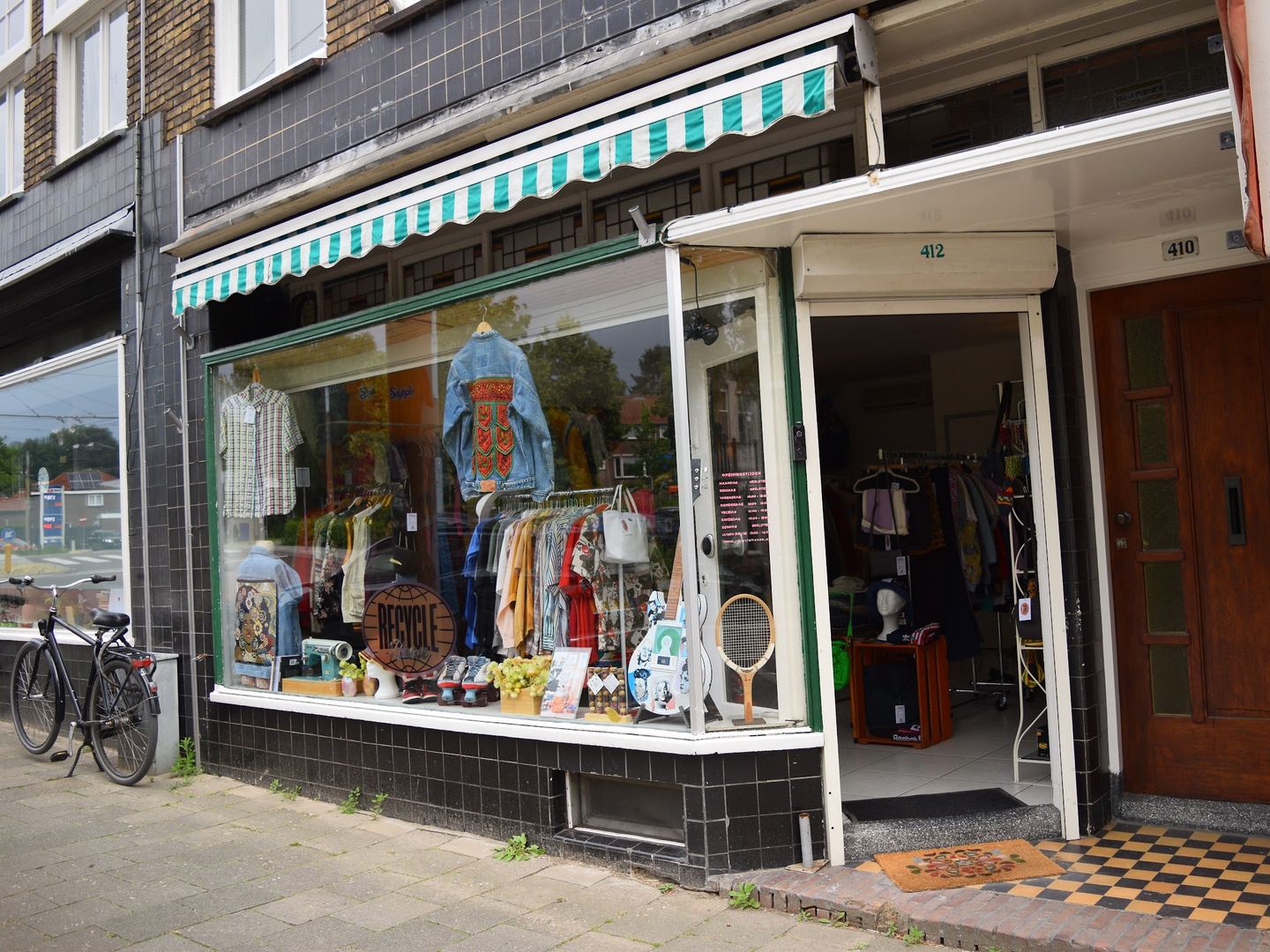 Winkelpui van Recycle House met groen-witte luifel en kleding in de etalage