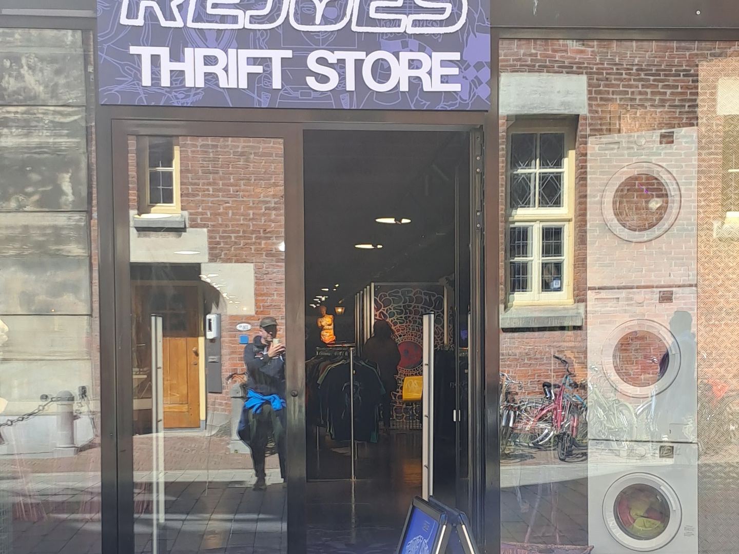 Ingang van Rejoes met paars naambord, open glazen deur en stoepbord