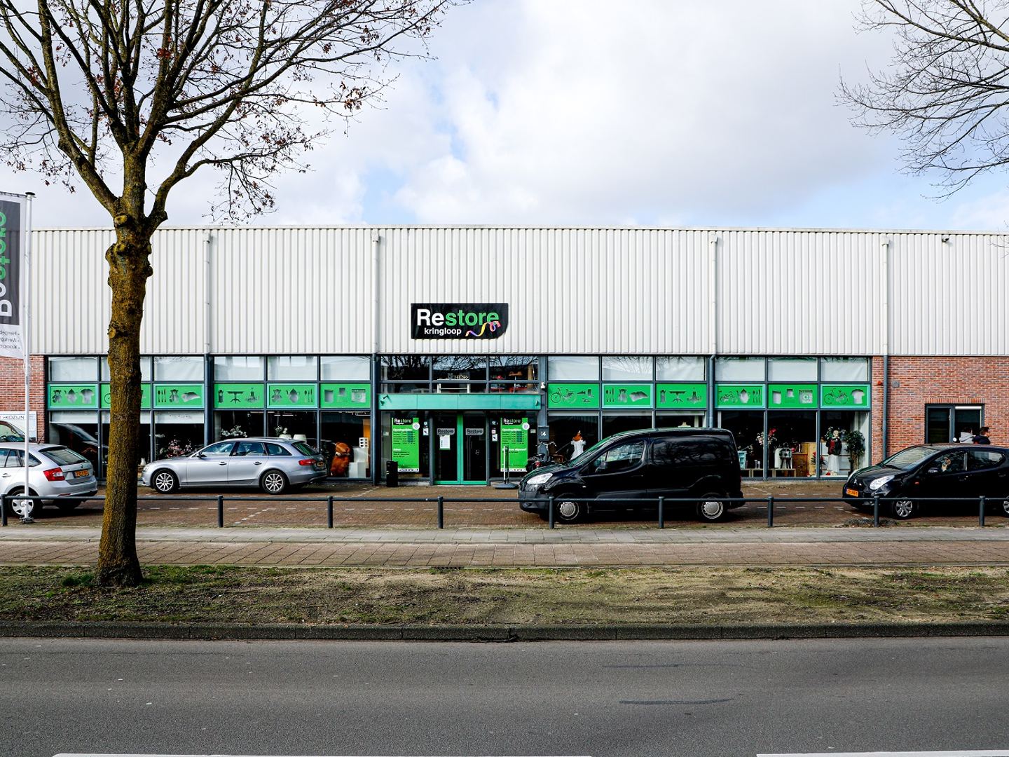 Winkelpand van Restore Kringloop Veenendaal met groen naambord, een rij groene etalageramen en parkeerplaatsen ervoor