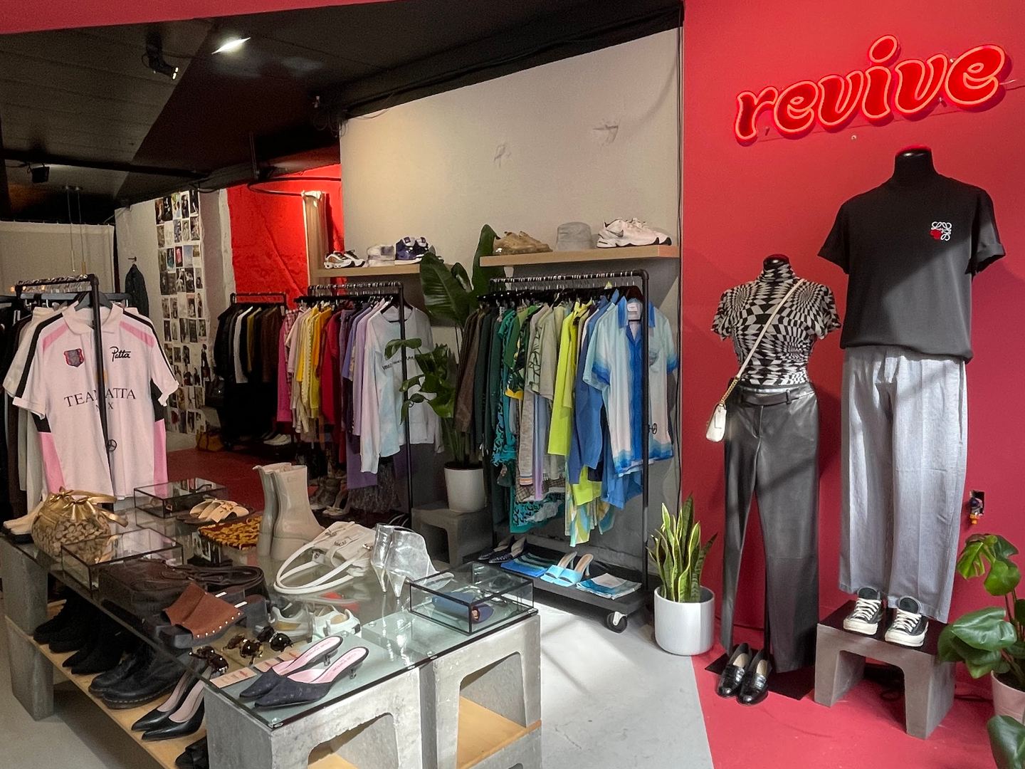 Interieur van Revive met rode wand, neonnaam, kledingrekken en schoenen op een tafel