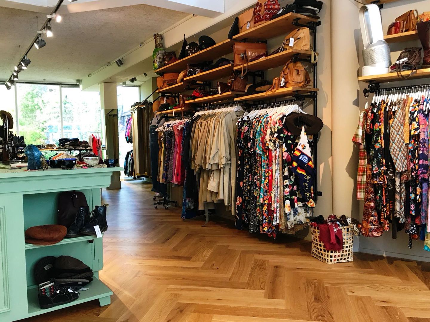 Interieur van Rumors Vintage & Design met rekken vintage kleding en tassen op houten planken