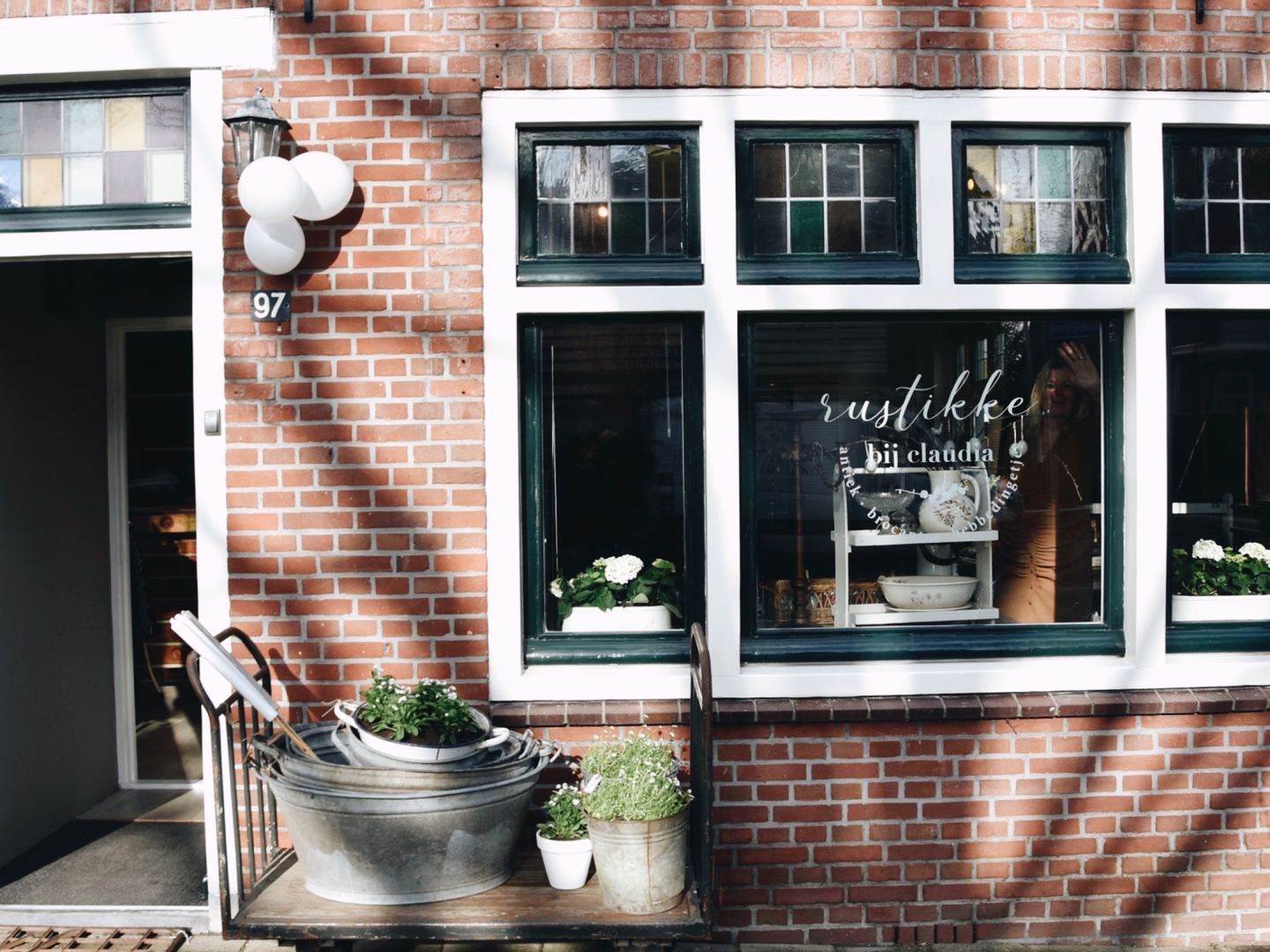 Gevel van Rustikke met belettering op het raam en een brocante karretje met planten bij de deur