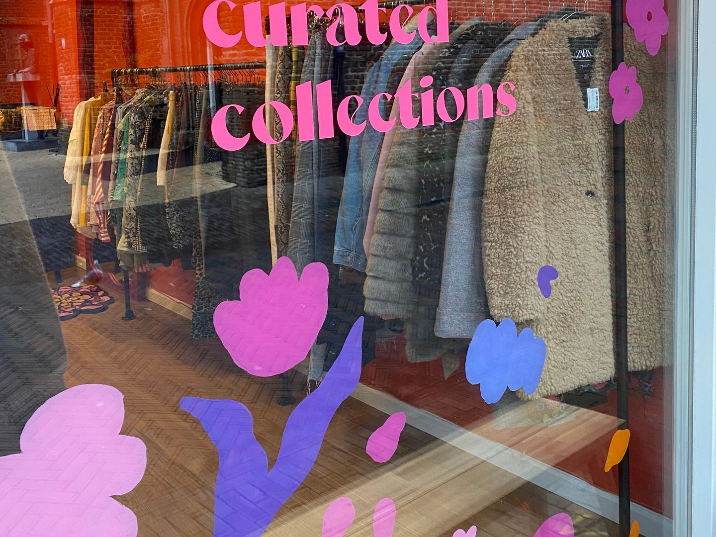 Etalageruit van Savvy Collectives met roze tekst preloved curated collections, bloemenstickers en een rek met jassen