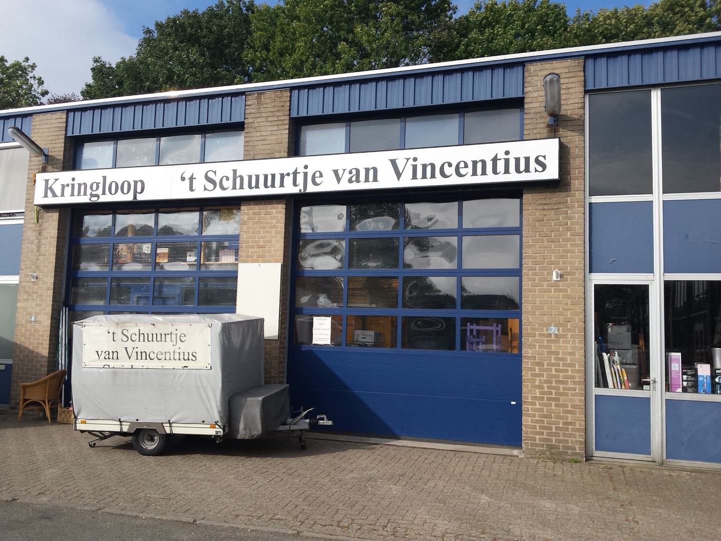 Gevel van Kringloop 't Schuurtje van Vincentius met naambord boven de garagedeuren
