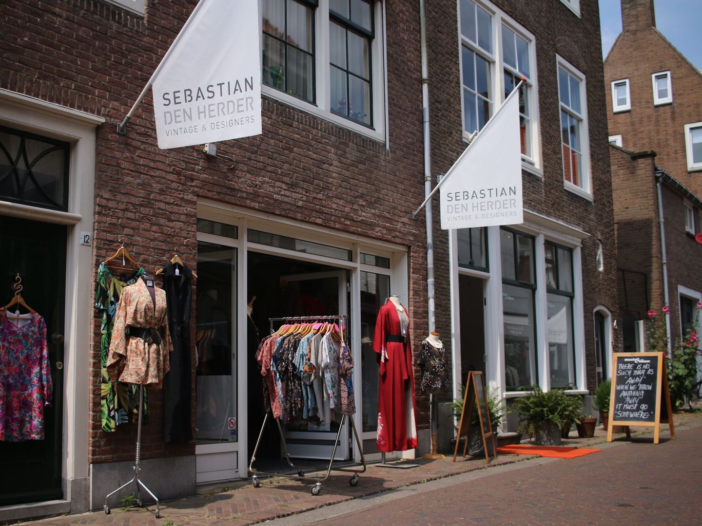 Gevel van Sebastian den Herder Vintage & Designers met naamvlaggen, kledingrekken en paspoppen bij de ingang