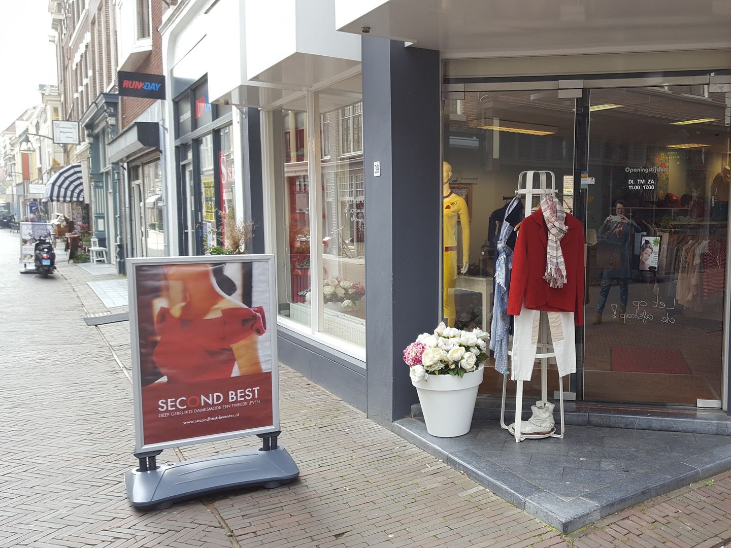 Winkelpui van Second Best op een straathoek met etalagepop, bloemen en een reclamebord