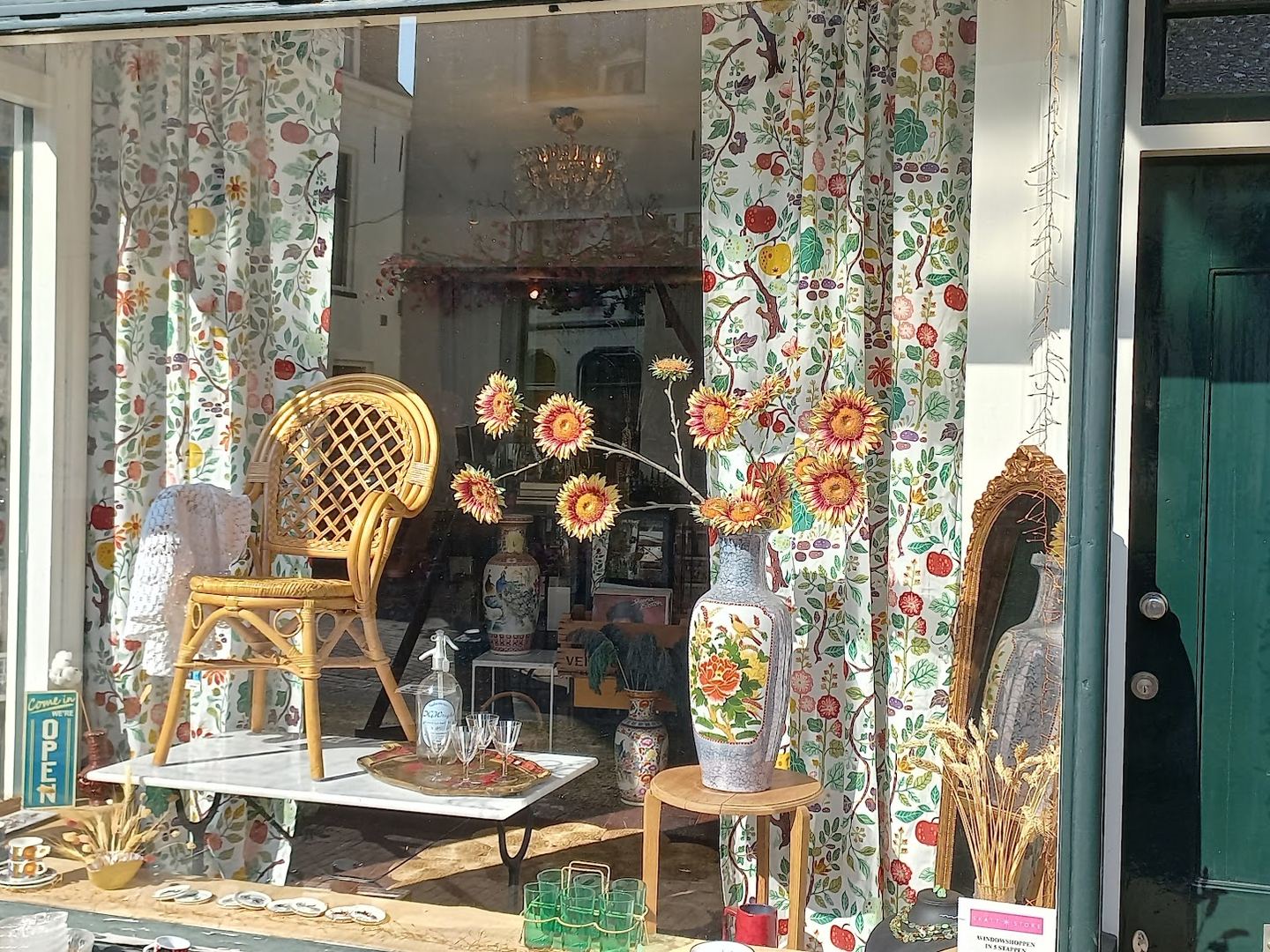 Etalage van SKATT STORE met een rieten stoel, bloemvazen en vintage woonaccessoires