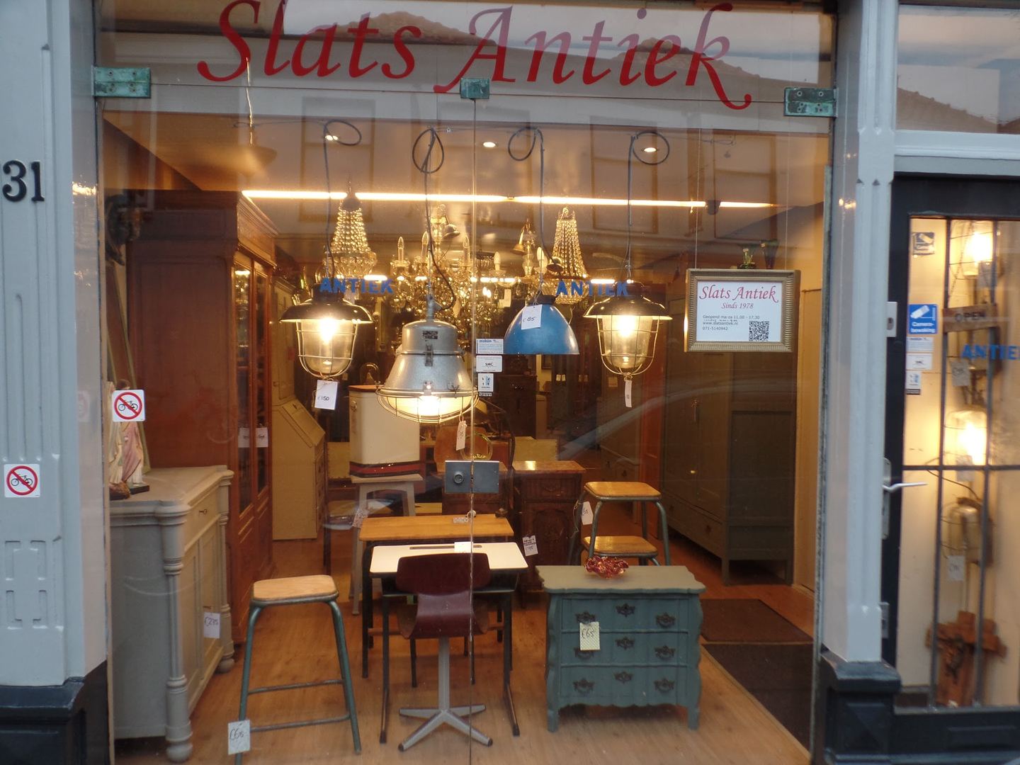 Etalage van Slats Antiek met de naam in rode letters, hanglampen en geschilderde kastjes achter het glas