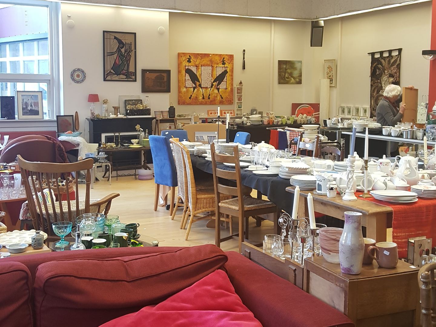 Interieur van SOEK Stichting Oegstgeester Kringloop met servies, stoelen en een rode bank