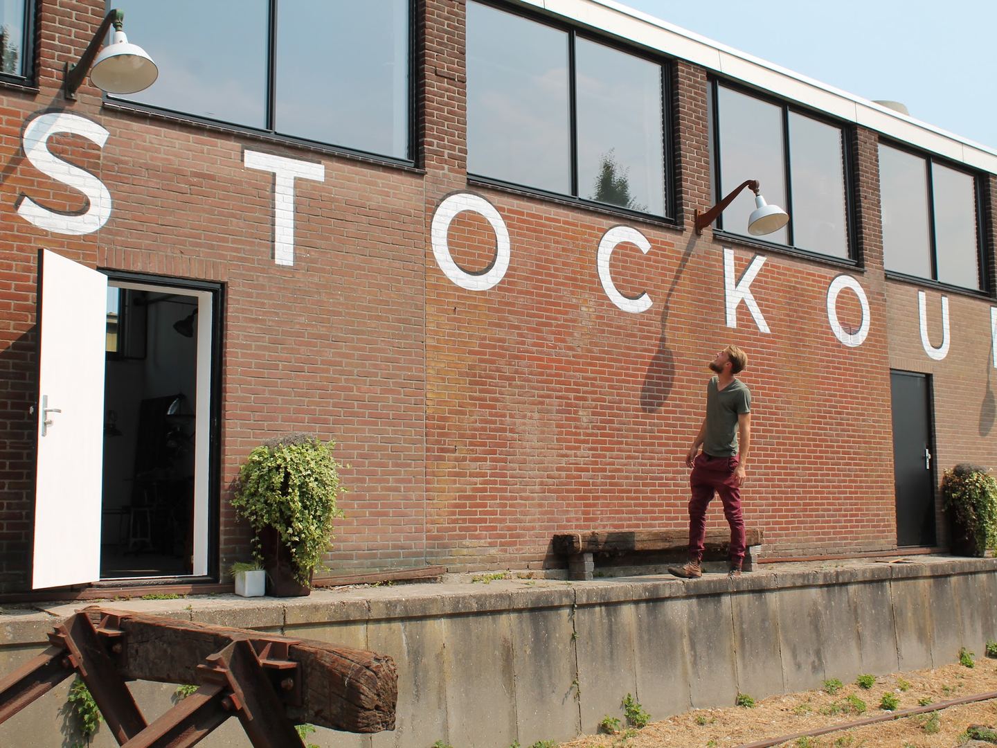 Bakstenen gevel van Stockoud met grote witte letters, industriële wandlampen en een openstaande ingangsdeur