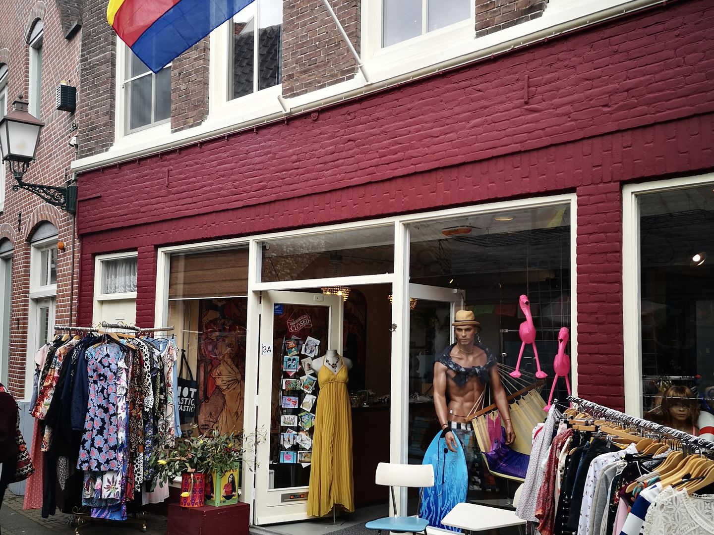 Rode winkelpui van 't Glop met kledingrekken buiten en etalagepoppen in de deuropening