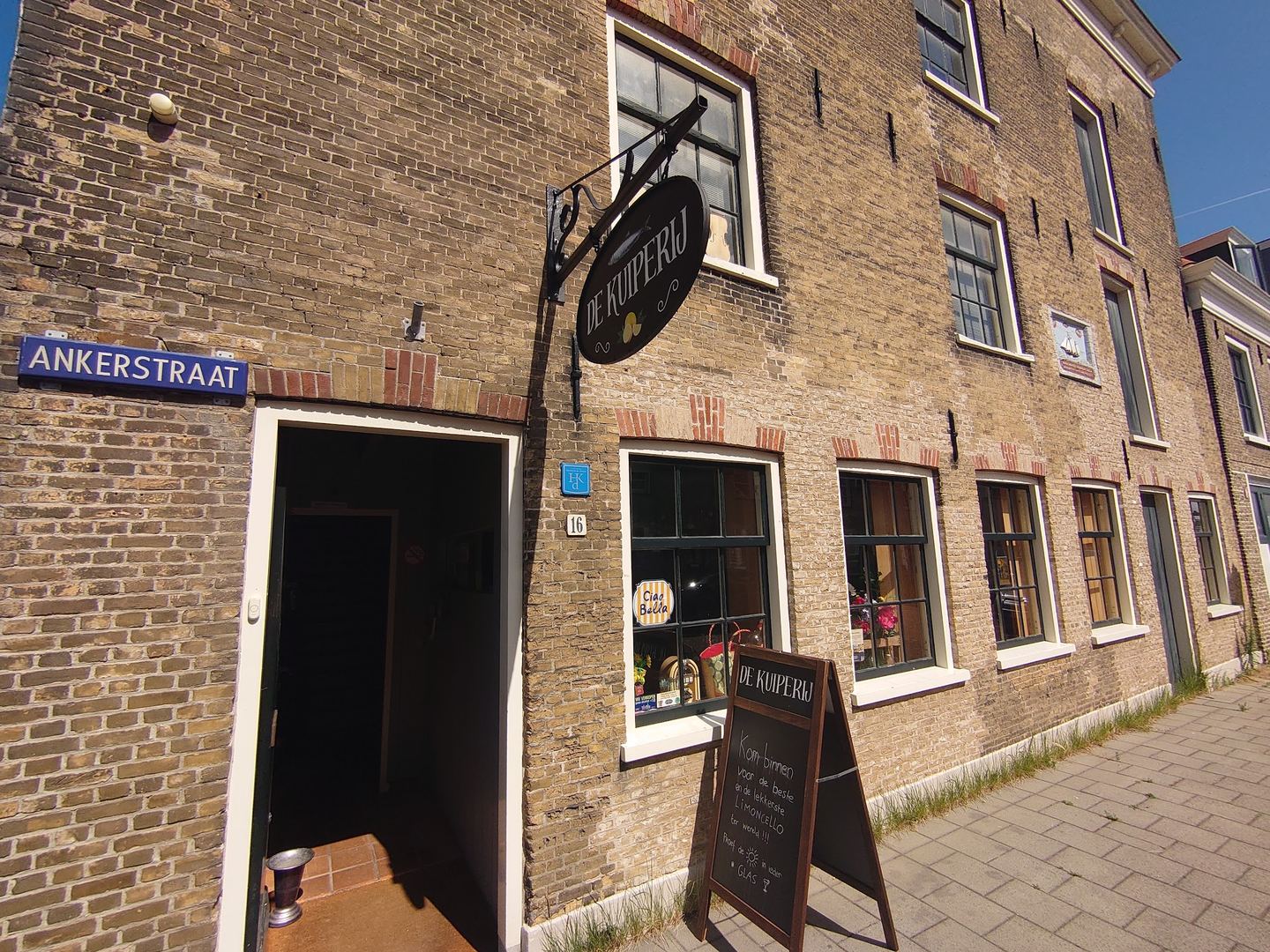 Gevel van De Kuiperij met uithangbord en open deur, waar 't Pakhuis vintage en brocante verkoopt
