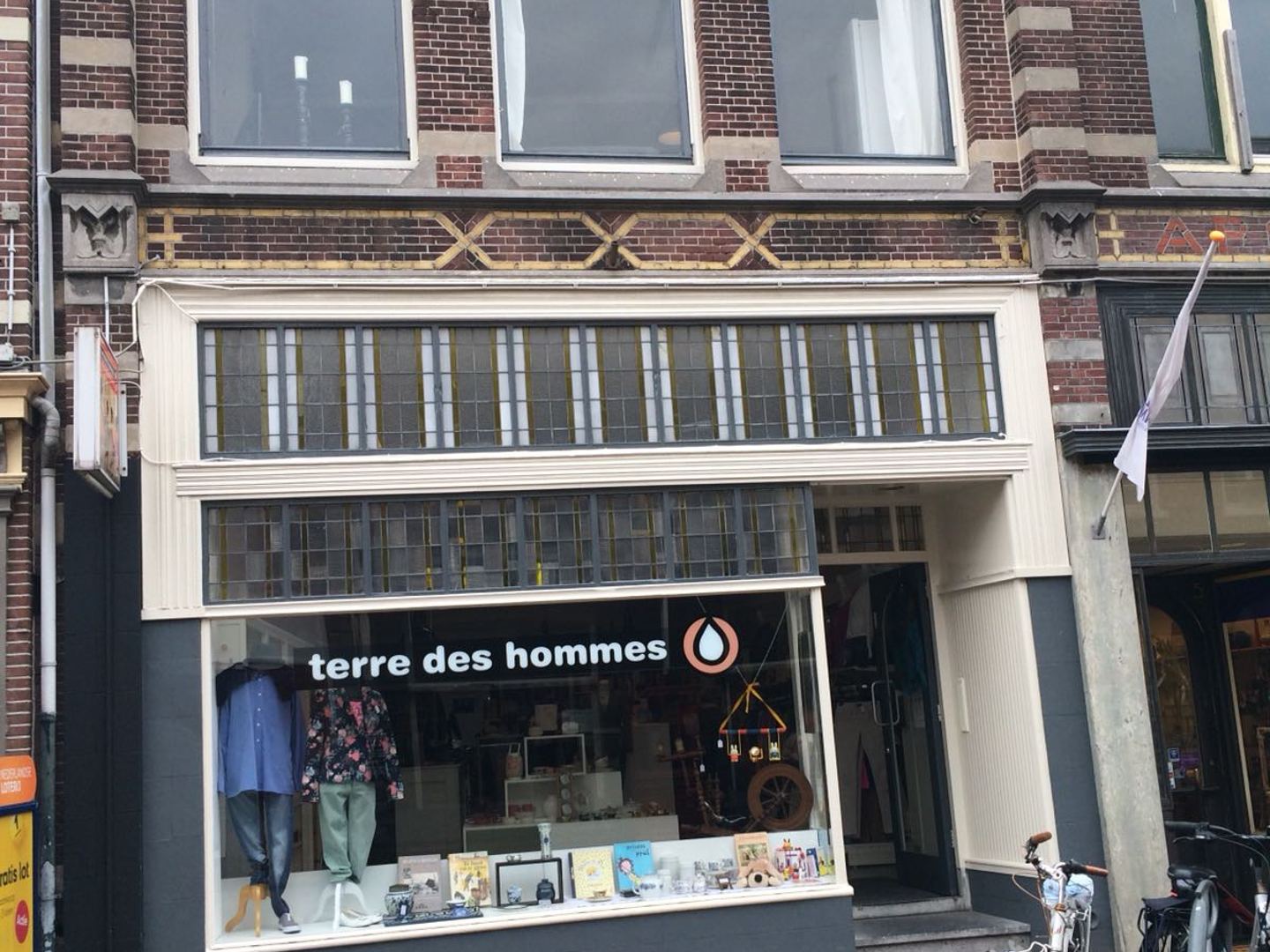 Gevel van de Terre des Hommes winkel met de naam op de etalage, kleding en boeken in het raam