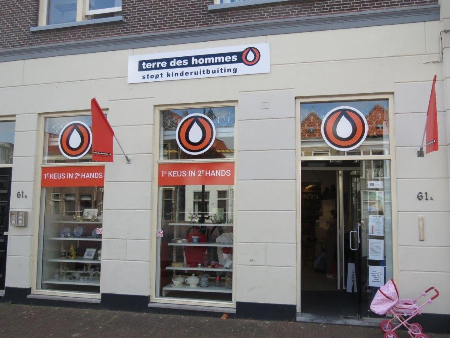 Lichte gevel van de Terre des Hommes-winkel met drie etalages vol tweedehands spullen