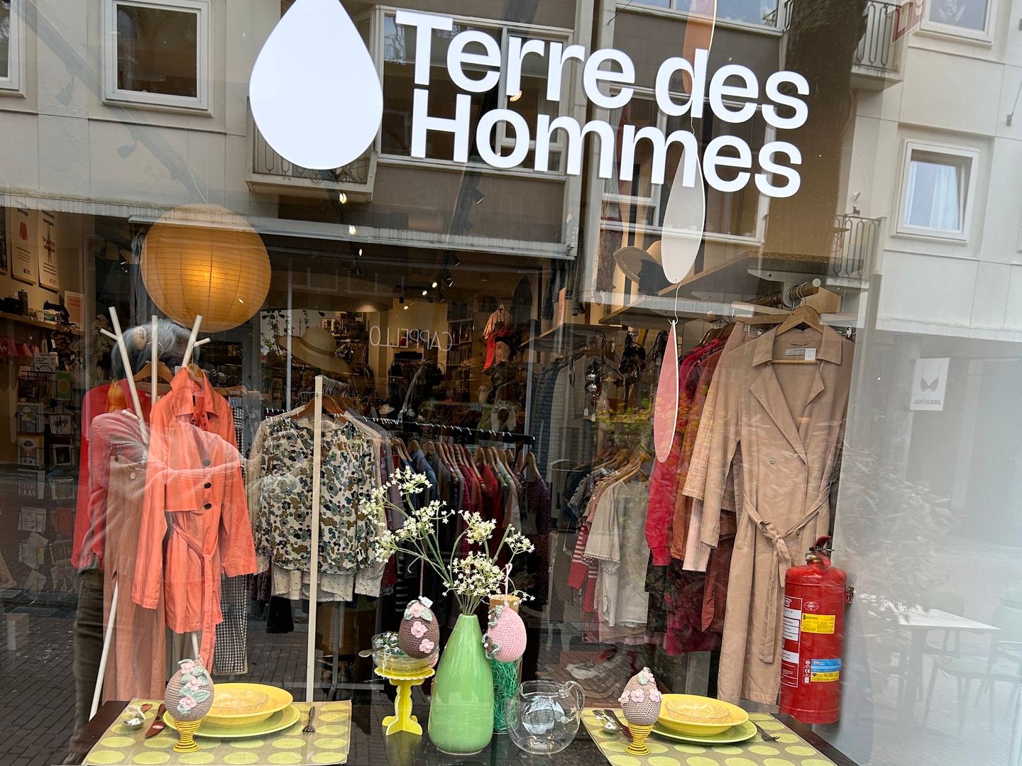Etalage van Terre des Hommes met het logo op het raam, kleding en woonaccessoires