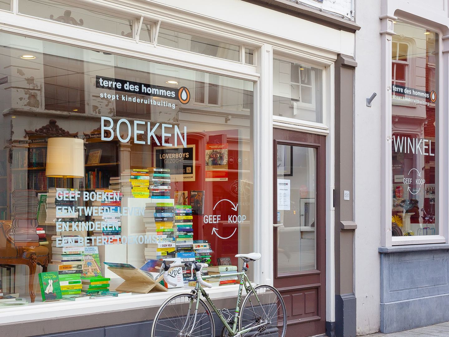 Winkelpui van Terre des Hommes met een etalage vol boeken en een fiets voor het raam