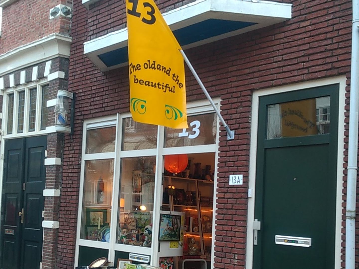 Gevel van The Old and The Beautiful met gele vlag en een bank met boeken en platen voor de etalage