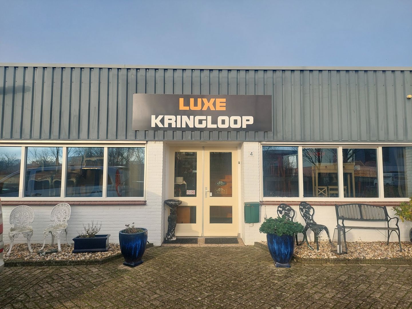 Gevel van de Luxe Kringloop met naambord en tuinmeubels voor de ingang