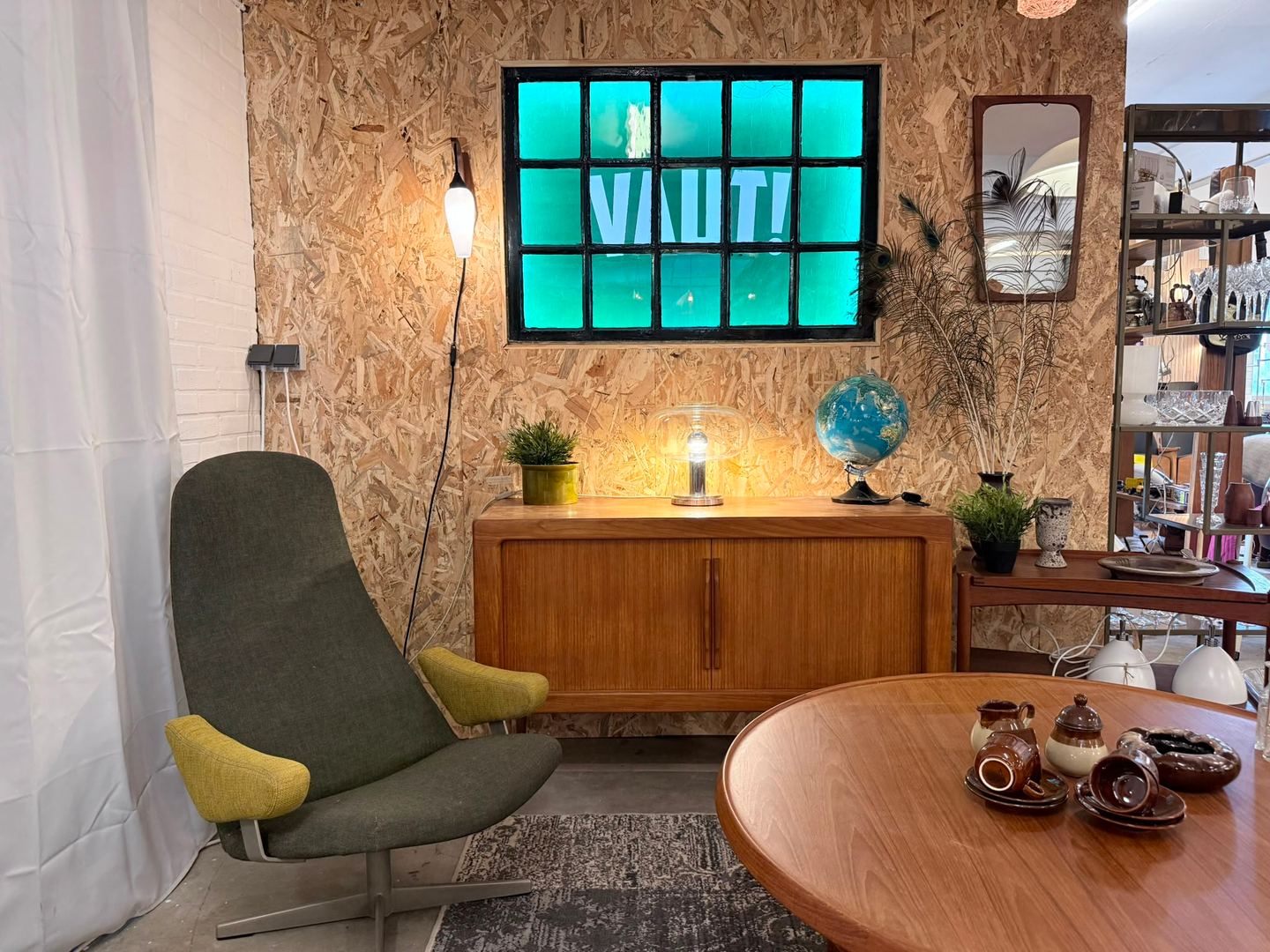 Showroomhoek van VAUT met verlicht groen raam met de naam, een teakhouten dressoir, groene fauteuil en tafellampen