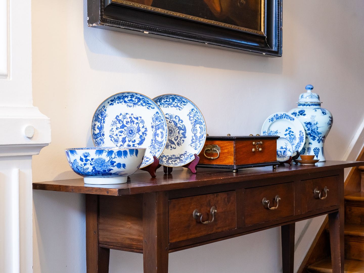 Antieke wandtafel met blauw-wit porselein en een houten kistje in het trappenhuis van Verkoulen Antiques