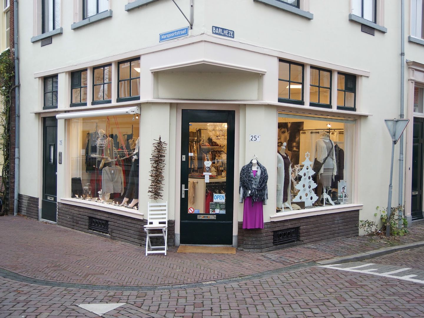 Wit hoekpand van Via Patries met etalages vol dameskleding