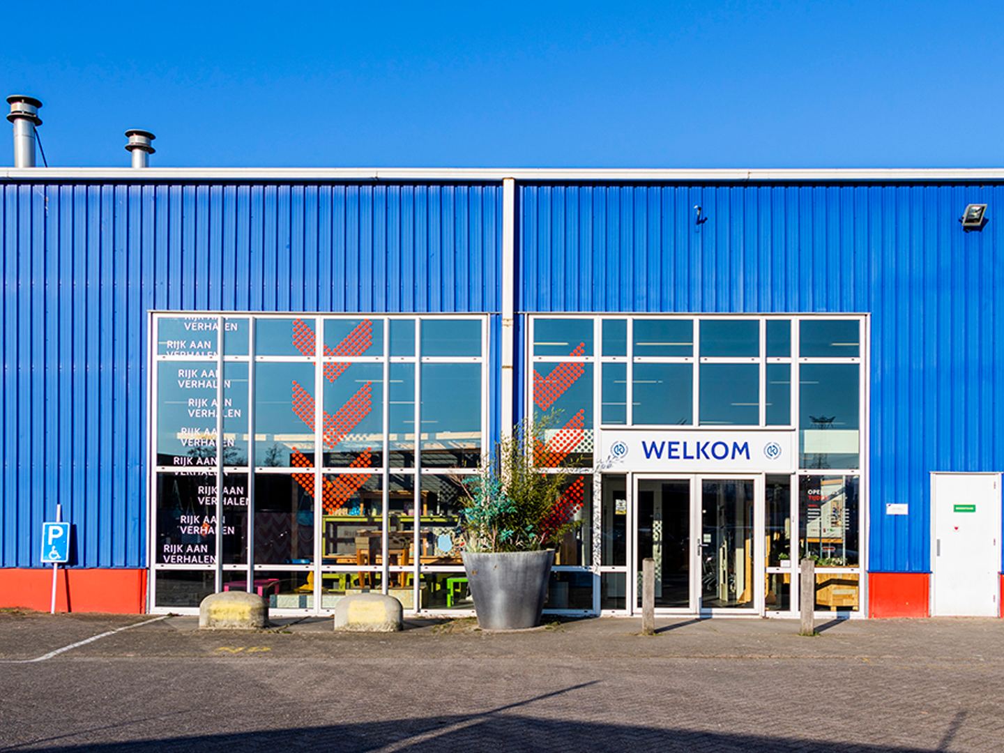 Blauwe gevel van Vindingrijk Kringloop met grote ramen en een welkomstbord boven de ingang