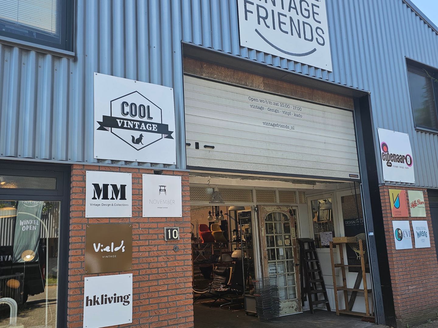 Gevel van de loods van Vintage Friends met de borden van de handelaren bij de ingang