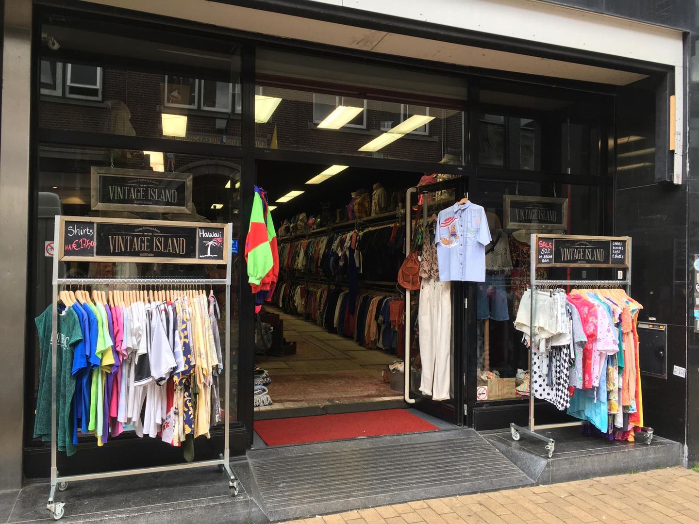 Open pui van Vintage Island met rekken vol kleurige T-shirts en overhemden voor de ingang