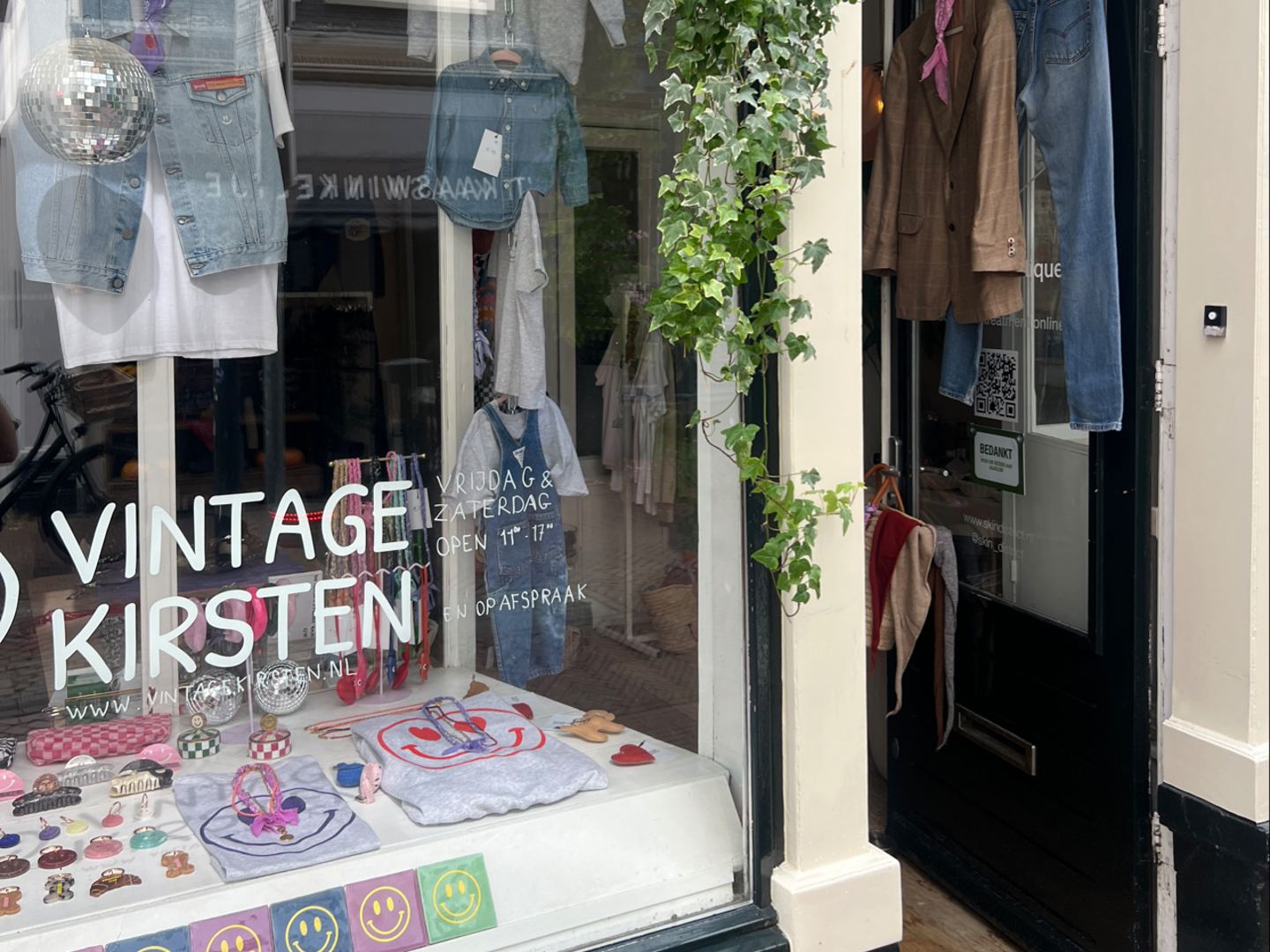 Etalage van Vintage Kirsten met spijkerjacks, smileykussens en de winkelnaam op het raam