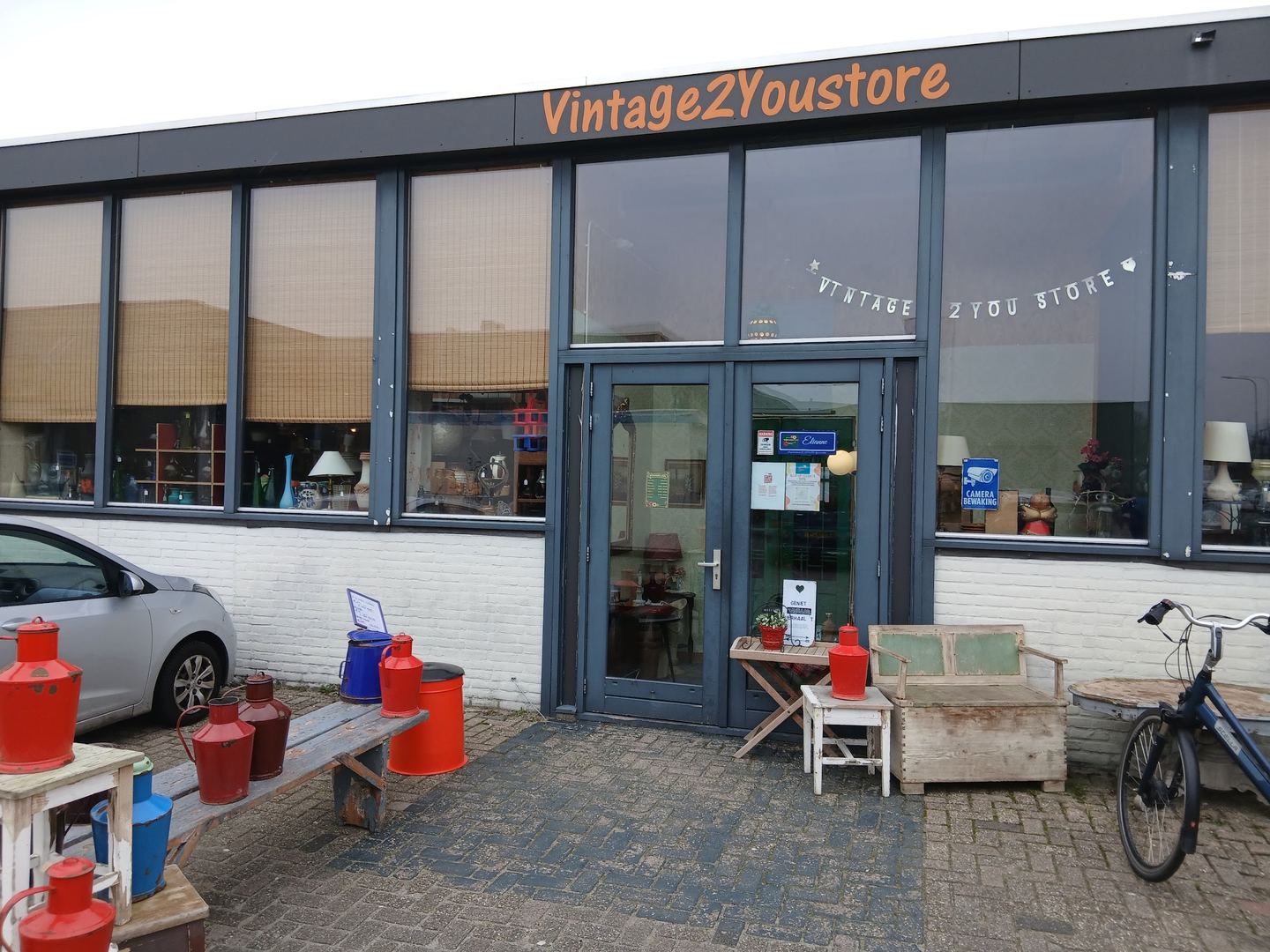 Gevel van Vintage2YouStore met emaille kannen en een houten bank voor de deur