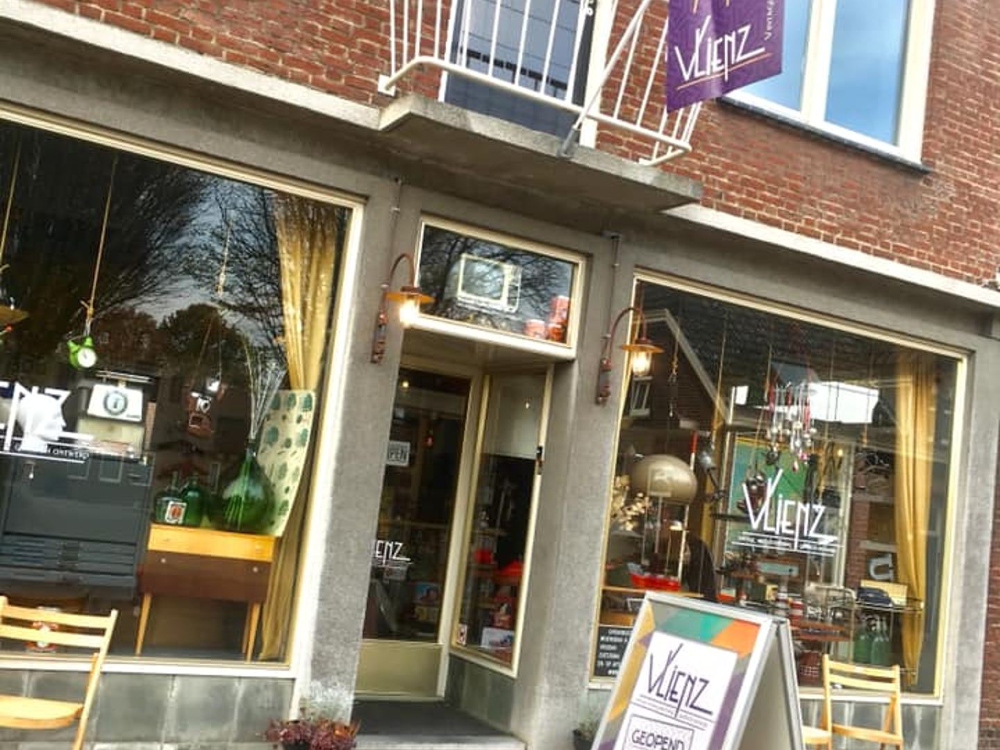 A brick building with a storefront, featuring large windows, an entrance, and a purple flag/sign.