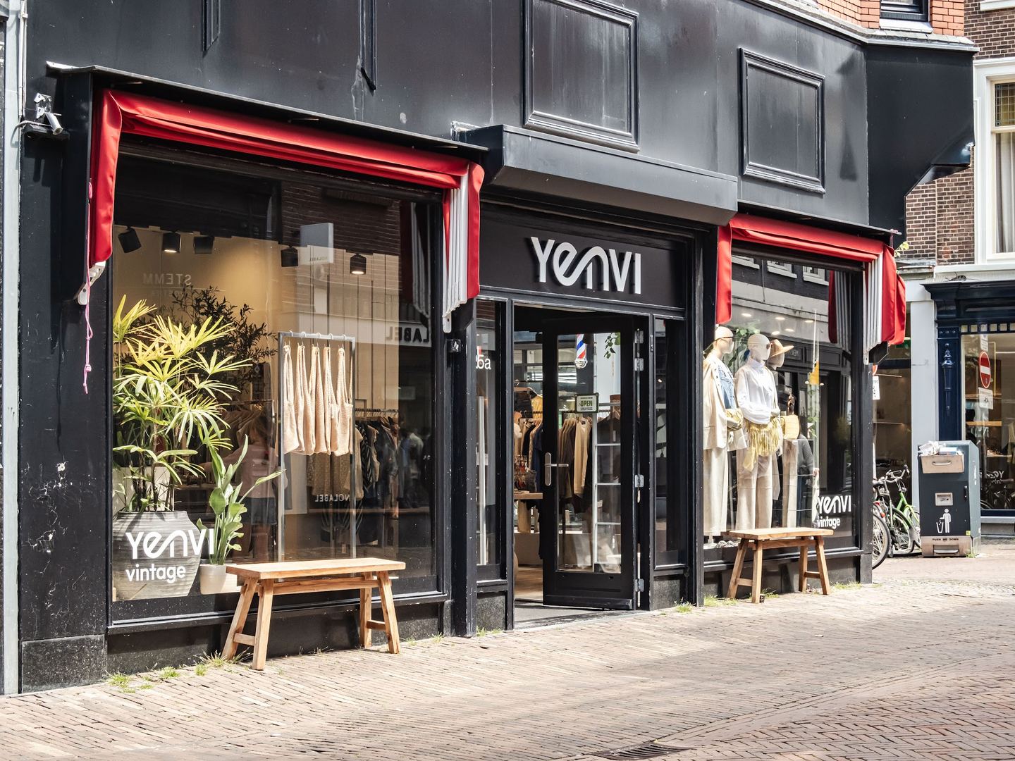 Zwarte gevel van Yenvi met rode luifels, etalagepoppen en een houten bankje voor de deur